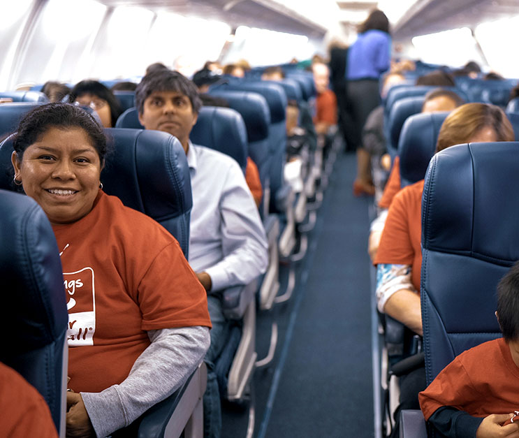View down the middle aisle of an airplane, with people sitting in seats and woman smiling in the foreground