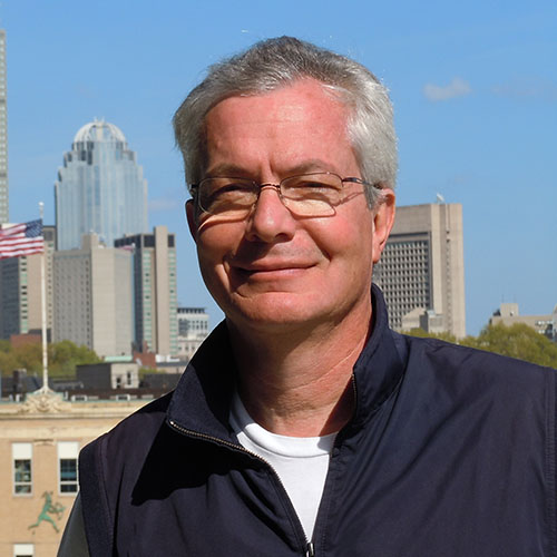 A man with glasses smiling in front of a city skyline