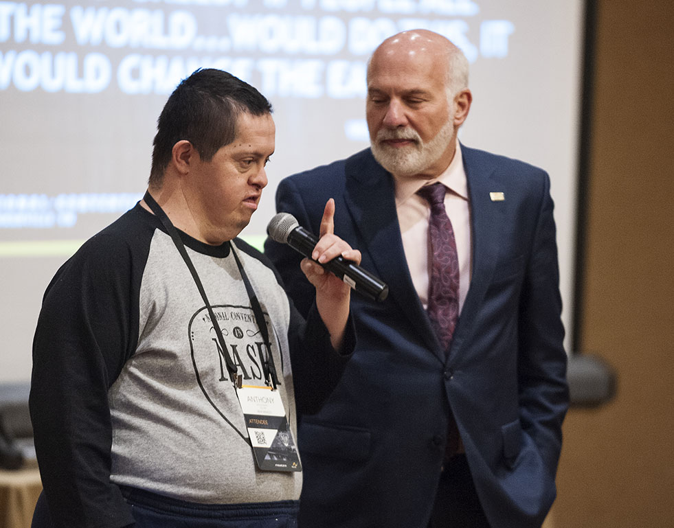 Man with Down syndrome speaks into microphone at The Arc's National Convention and stands beside The Arc CEO Peter Berns
