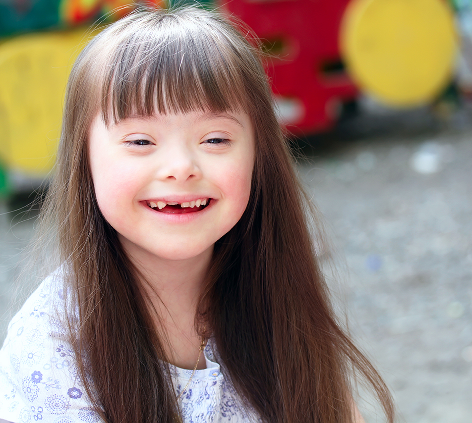 Portrait of a smiling young girl with Down syndrome at a playground.