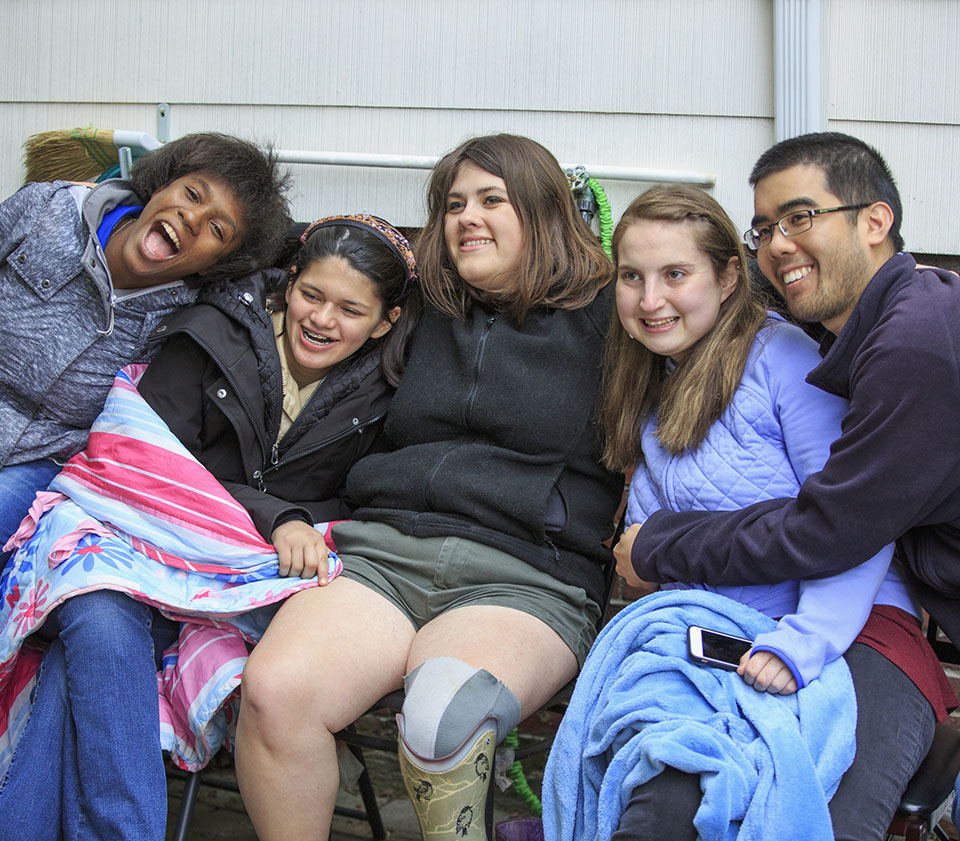 Group of smiling teenagers sitting outdoors with blankets