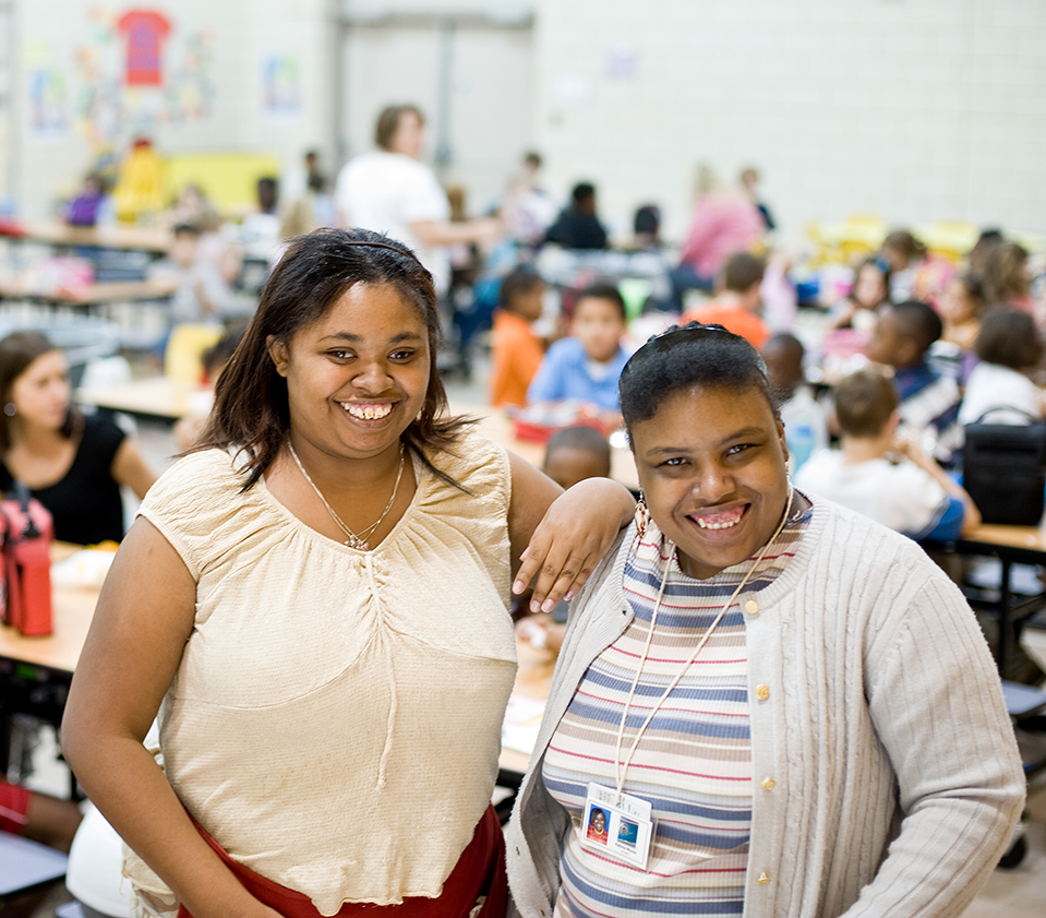 Two smiling women with disabilities standing in a school cafeteria