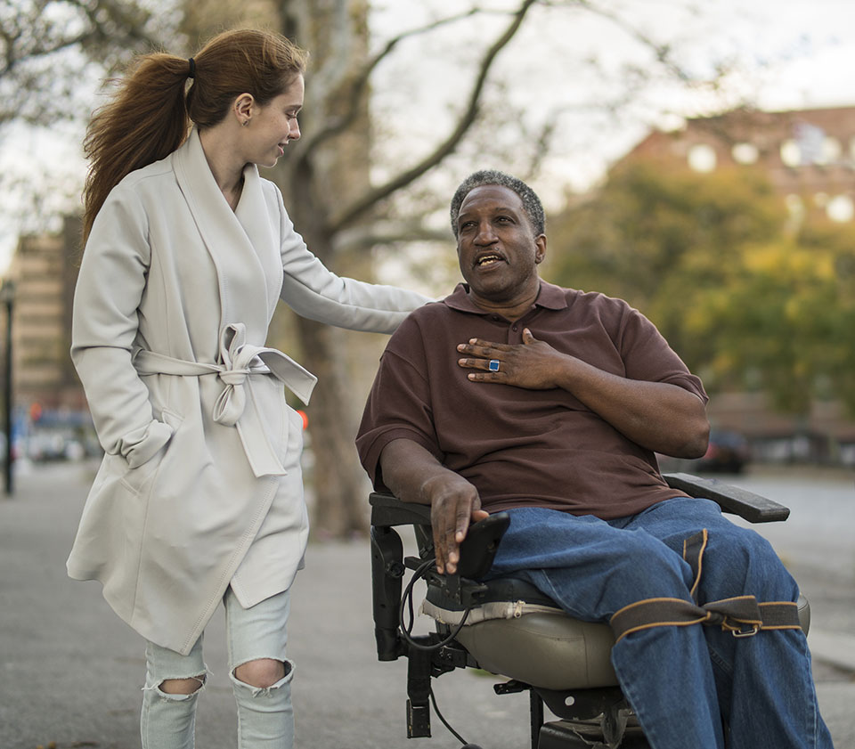 Young woman talking with man in wheelchair as they walk together outside
