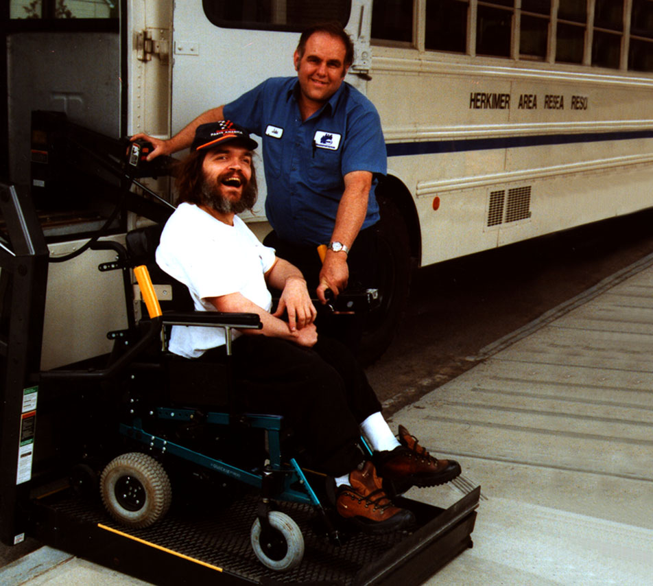 Bearded man sitting on wheelchair that's being lowered off a bus